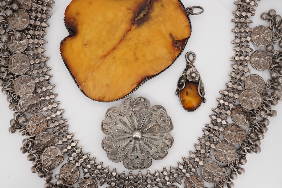 An Indian white metal fringe necklace, 37.5cm, a large antique white metal mounted amber pendant(a.f.), one other later smaller amber pendant and a filigree brooch. Condition - poor to fair